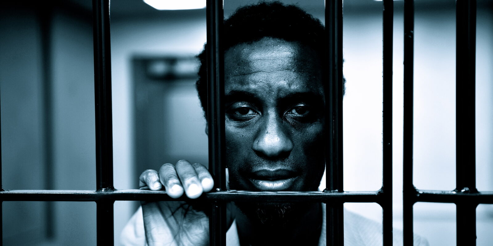 Clint Dyer as Delroy behind the bars of a cell