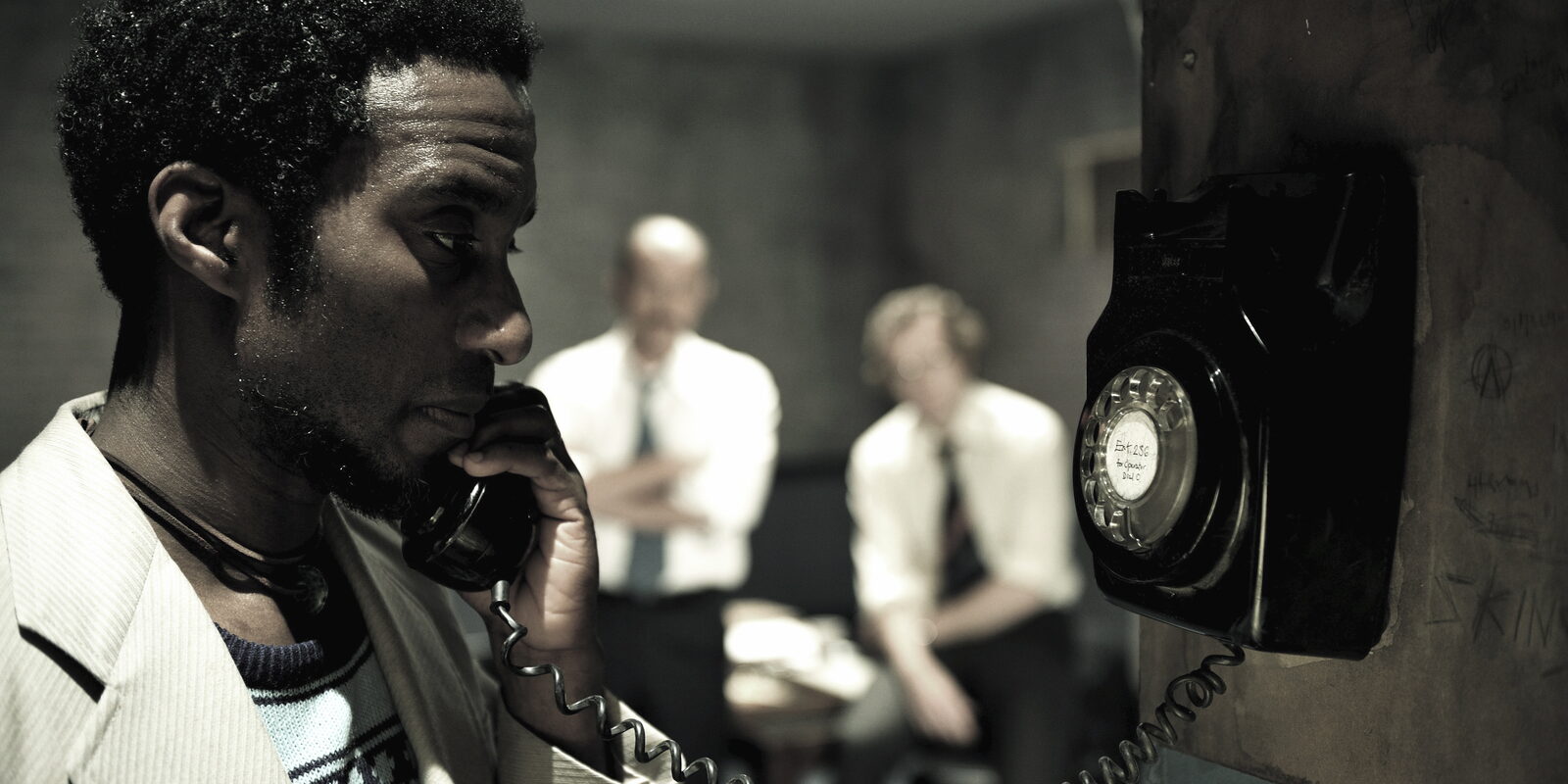 Clint Dyer as Delroy on the station telephone, the two officers behind him