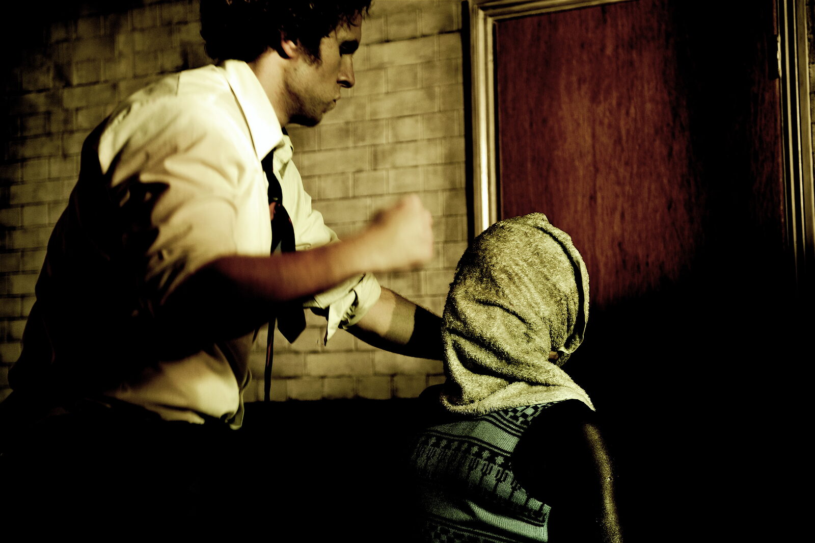 Rafe Spall as DC Wilby attacking a hooded prisoner